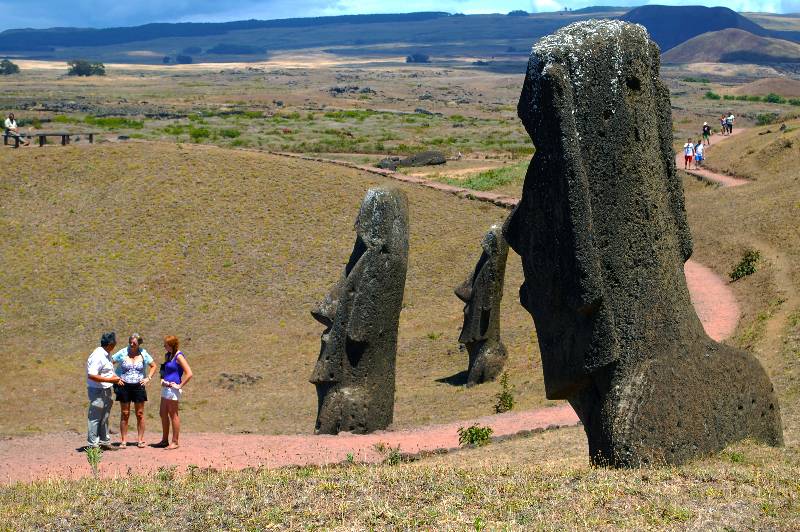 Three tourists standing across 3 moais embedded on the ground in Rano Raraku quarry
